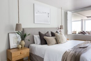 Une chambre à coucher avec un lit, des tables de chevet, une lampe suspendue, un tableau encadré et une fenêtre donnant sur un paysage.