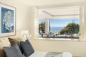 Enjoy ocean views from the balcony, featuring a sofa and chairs, and relax in the spacious bedroom with a large window.