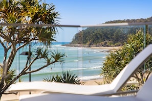 Enjoy the serene ocean views from this beachfront balcony, surrounded by lush greenery and a forested hillside.