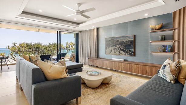 Una sala moderna con un sofá, una mesa de centro y un televisor. Tiene un balcón con vista al mar.