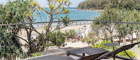 A balcony with lounge chairs overlooking a beach and ocean.