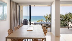 Un comedor moderno con una mesa grande y sillas, vistas al mar y un balcón con mobiliario exterior.