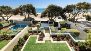 Zona de piscina con vista a la playa, rodeada de vegetación y un cielo despejado.
