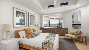 Un dormitorio moderno con cama, mesitas de noche, zona de estar y vistas al mar.