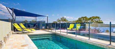 A swimming pool with clear blue water, surrounded by lounge chairs and a shaded area.