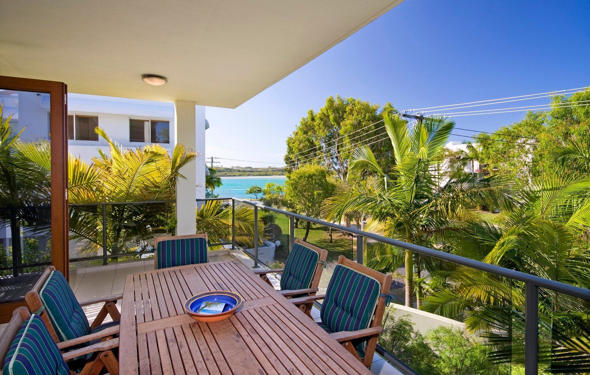 Une table en bois, entourée de chaises, sur un balcon donnant sur une plage.
