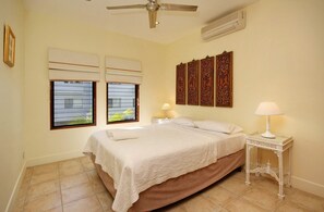 A bedroom with a bed, two bedside tables with lamps, a ceiling fan, and decorative wall panels.