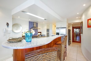 A modern kitchen with a curved island, a built-in oven, and a stainless steel refrigerator.