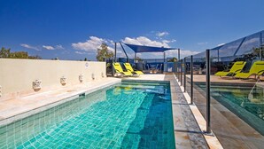 A swimming pool with sun loungers and a covered seating area.