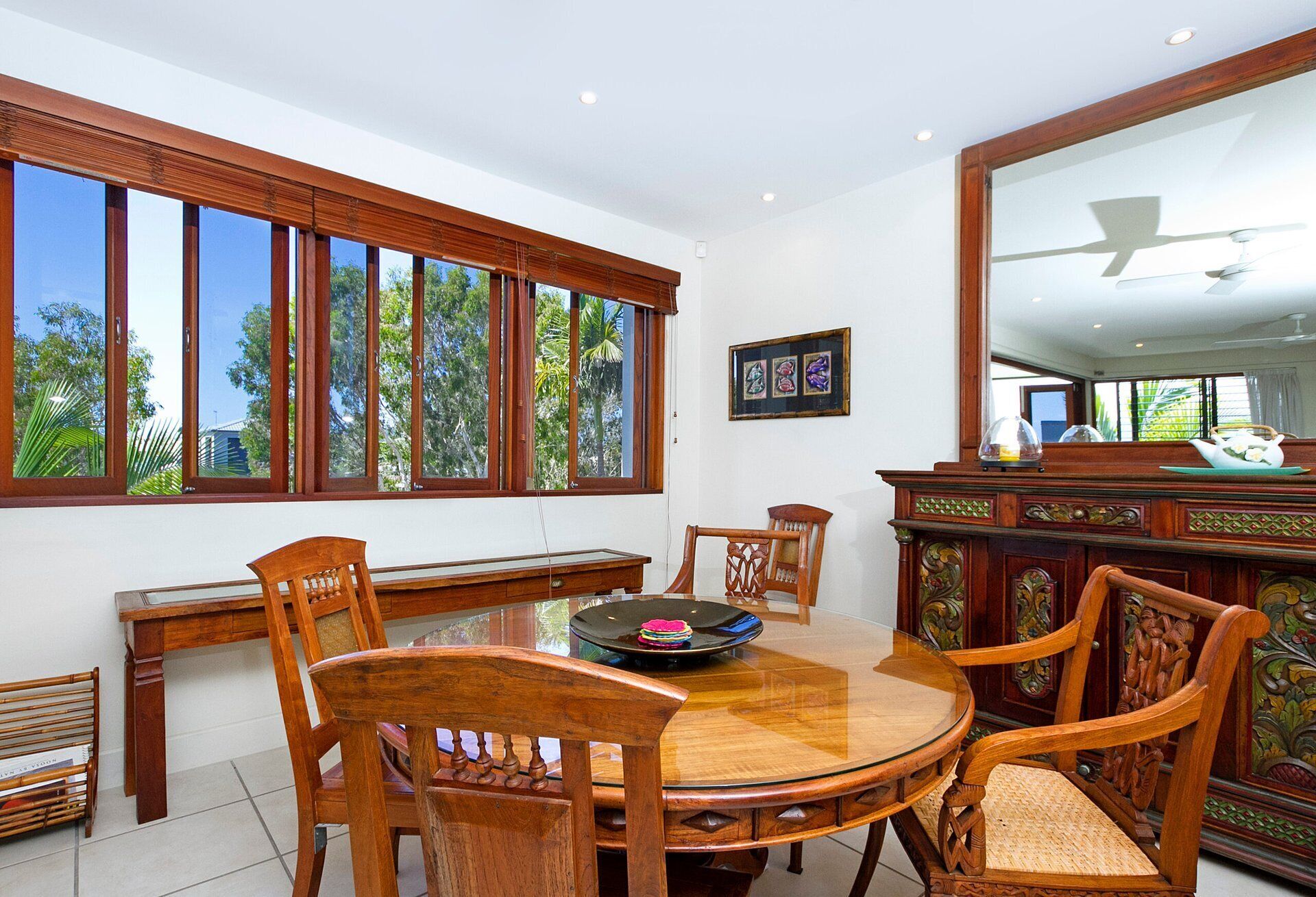 A dining area with a round glass table, wooden chairs, and a large window with multiple panes.