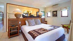 A hotel room with a large bed, a wooden headboard, a bedside table, a chair, a mirror, and a ceiling fan.