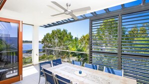 A dining area with a table and chairs, a ceiling fan, and a view of the sea through large windows.