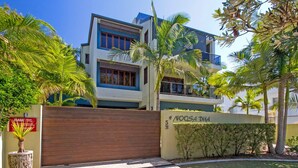 A modern multi-story building with a gated entrance, surrounded by palm trees and a well-maintained lawn.