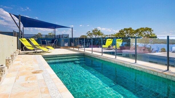 A swimming pool with clear blue water, surrounded by lounge chairs and a shaded area. - Noosa Dua 2 - Balinese Retreat (Noosaville)