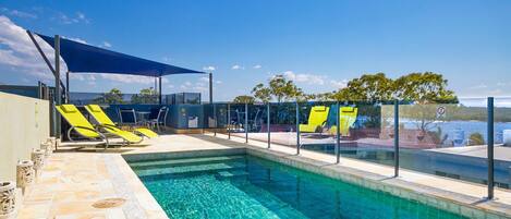 A swimming pool with clear blue water, surrounded by lounge chairs and a shaded area.