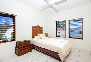 A bedroom with a bed, a wooden headboard, a bedside table, and two windows with blinds.