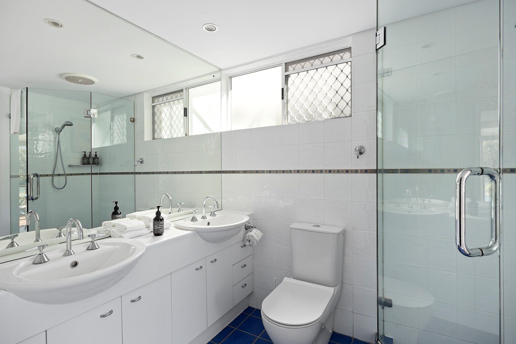 A modern bathroom with a glass shower enclosure, two sinks, a toilet, and a large mirror.