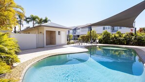A swimming pool with a curved edge, surrounded by a patio area with lounge chairs and a covered seating area. - Noosa Haven Apt 6 - Riverside Retreat (Noosaville)