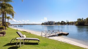 A waterfront property with a grassy area, a lounge chair, a small table, and a dock extending into the water. - Noosa Haven Apt 6 - Riverside Retreat (Noosaville)