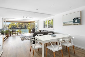 A modern interior with a dining area, a sofa, and a view of a lake.