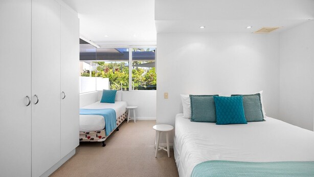 A modern bedroom with a bed, two bedside tables, a wardrobe, and a window with a view of greenery. - Noosa Haven Apt 6 - Riverside Retreat (Noosaville)