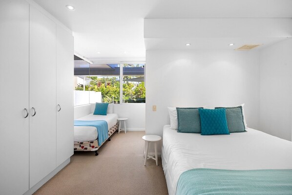 A modern bedroom with a bed, two bedside tables, a wardrobe, and a window with a view of greenery.