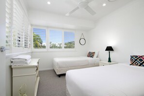 A hotel room with two beds, a window with blinds, a bedside table with a lamp, and a ceiling fan.