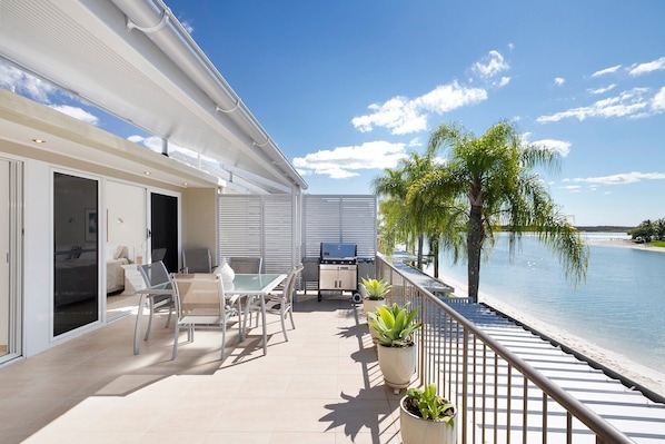 A balcony with a dining area, a grill, and a view of the water.