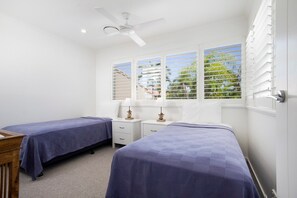 Camera da letto con due letti, ventilatore a soffitto e finestre con tende.