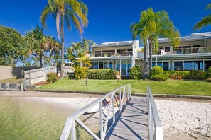 A beachfront property with a wooden deck leading to a sandy beach, a two-story building with a balcony, and palm trees.
