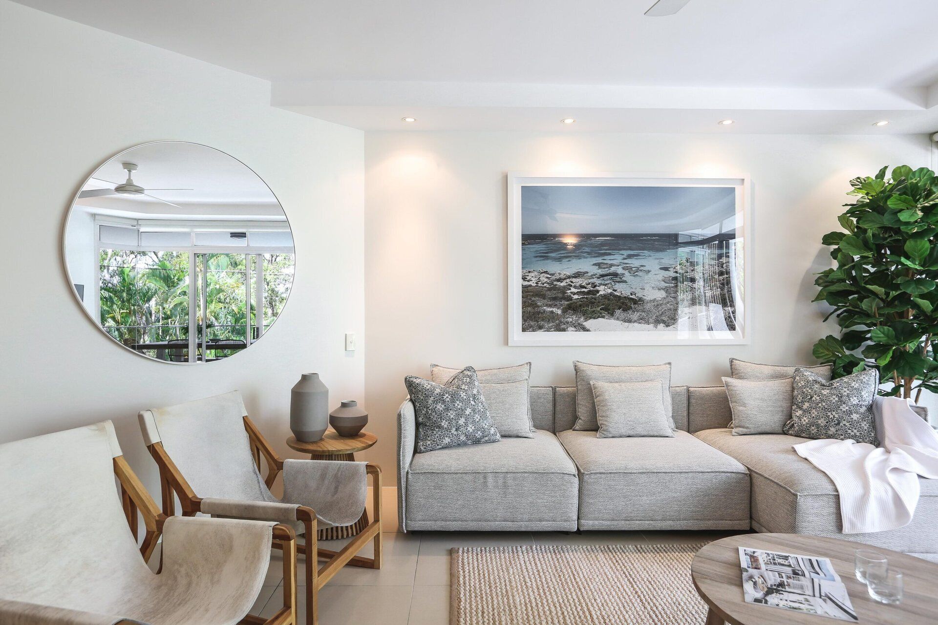 A modern living room with a sofa, chairs, a round mirror, and a large framed picture on the wall.