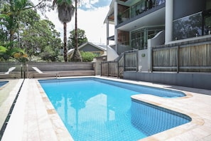 A swimming pool with a tiled edge, surrounded by a wooden fence and a building with balconies.