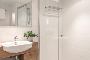 A bathroom with a white sink, a mirror, a glass shower enclosure, and a towel rack.