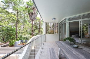 A balcony with a view of trees, a staircase, and a dining area with a table and chairs.