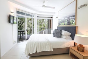 A bedroom with a bed, a nightstand, a lamp, a ceiling fan, a TV, and a sliding glass door leading to an outdoor area.