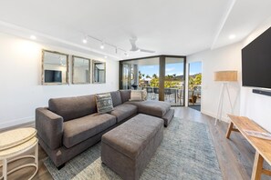 Un salon moderne avec un canapé d’angle, une petite table ronde et une grande fenêtre donnant sur l’extérieur.