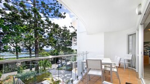 Een balkon met een tafel en stoelen, met uitzicht op een weg en groen.