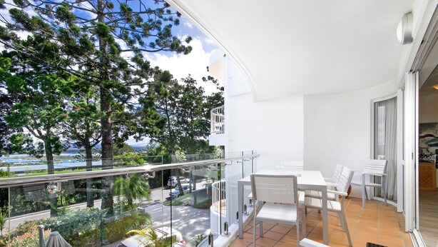 A balcony with a table and chairs, overlooking a road and greenery. - Nature's Haven Coastal Escape (Noosa Heads)
