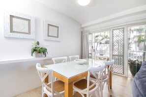 A dining area with a glass-top table, white chairs, and a potted plant. - Nature's Haven Coastal Escape (Noosa Heads)