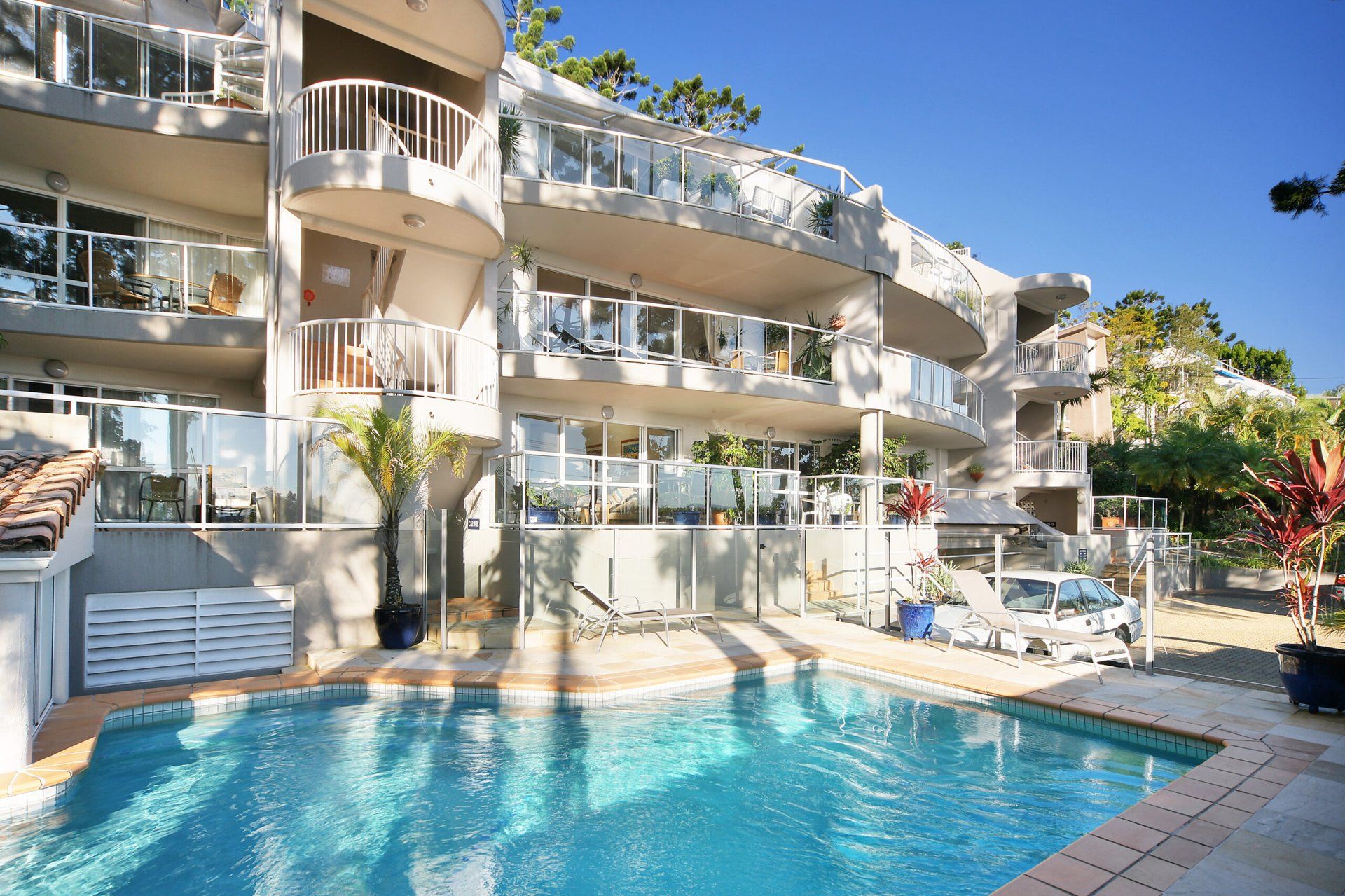 A multi-story hotel with a swimming pool, balconies with railings, and potted plants.
