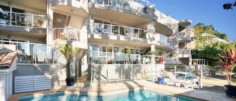 A multi-story hotel with a swimming pool, balconies with railings, and potted plants.