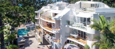 A multi-story hotel with balconies, a pool, and lush greenery.