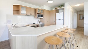 A modern kitchen with a central island, bar stools, and built-in appliances. - Nature's Haven Coastal Escape (Noosa Heads)