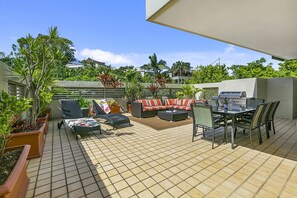 Relax outdoors with a sofa, dining table, and grill, surrounded by lush greenery.