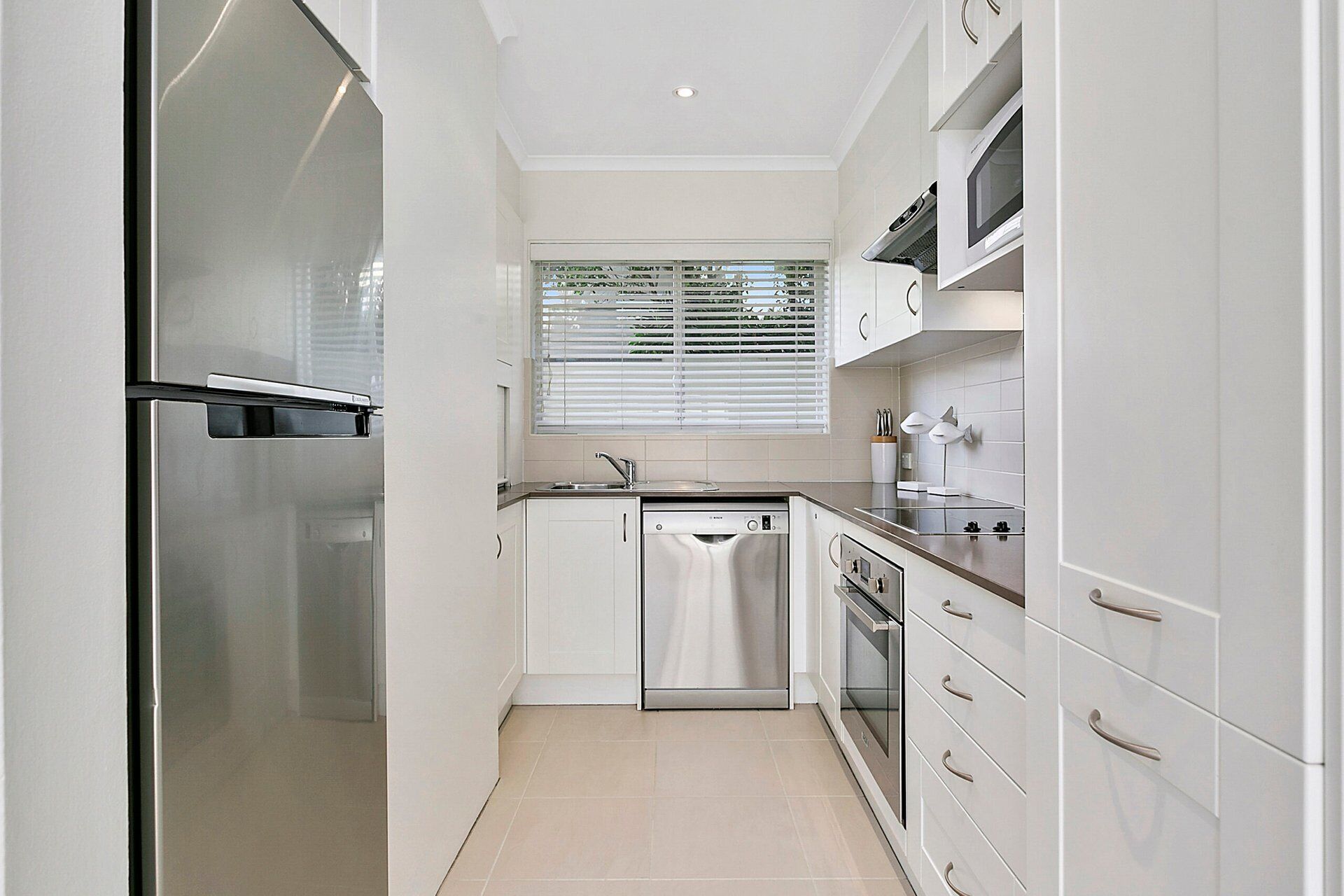 A modern kitchen with stainless steel appliances, white cabinetry, and a window with blinds.