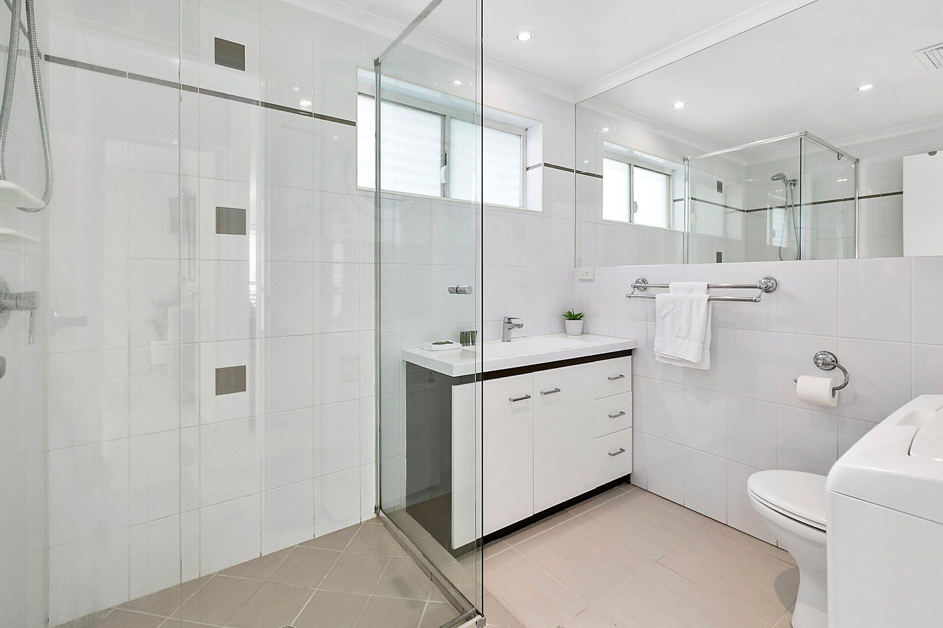 Une salle de bain moderne avec une douche à parois de verre, un lavabo blanc avec un miroir au-dessus et des toilettes.
