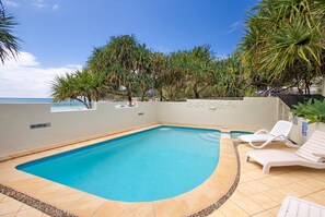 A swimming pool with a tiled edge, surrounded by lounge chairs and tropical plants.