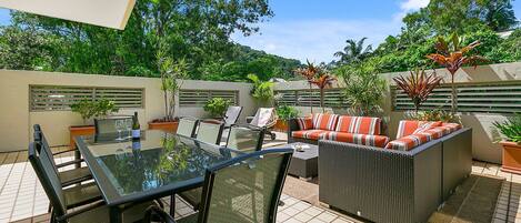An outdoor patio with a glass-top table, chairs, and a sofa with striped cushions.