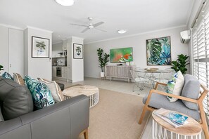 A modern living room with a grey sofa, a dining area with a white table, and a kitchen in the background.