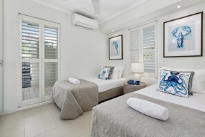 A hotel room with two beds, a large window with blinds, an air conditioning unit, and framed artwork on the wall.